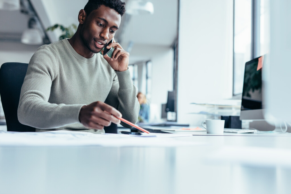 Image of a guy on his phone looking at a document with a pencil in hands 